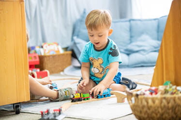 A young student playing with a wooden train set