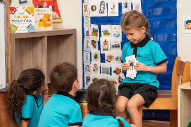Students participating in a literacy learning activity at NAS Dubai, with one child sharing materials while classmates listen during an early years classroom session.
